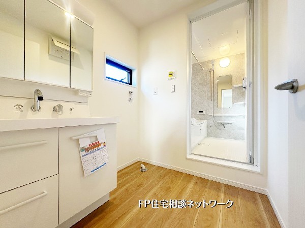 三面鏡収納を備えた使い勝手の良い洗面化粧台。奥には清潔感ある浴室が続き、家事導線もスムーズ。毎日の身支度が快適になる水回り設備です。