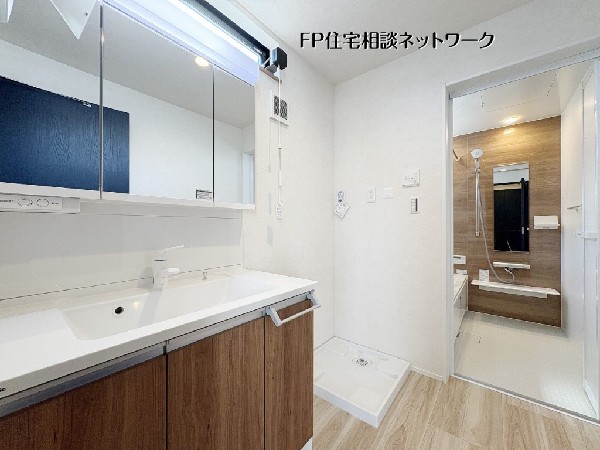 【洗面脱衣室】  木目調のパネルが落ち着いた雰囲気を醸し出す、清潔感あふれる洗面化粧台とバスルーム。三面鏡裏の収納や広々とした洗面ボウルなど、機能性も兼備しています。