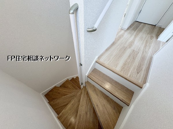 【階段】  木の温もりが感じられるナチュラルな色合いの階段スペース。手すりが設置されており、日々の昇り降りにも配慮された設計です。白を基調とした壁紙が光を反射し、明るく清潔感のある住空間を演出しています