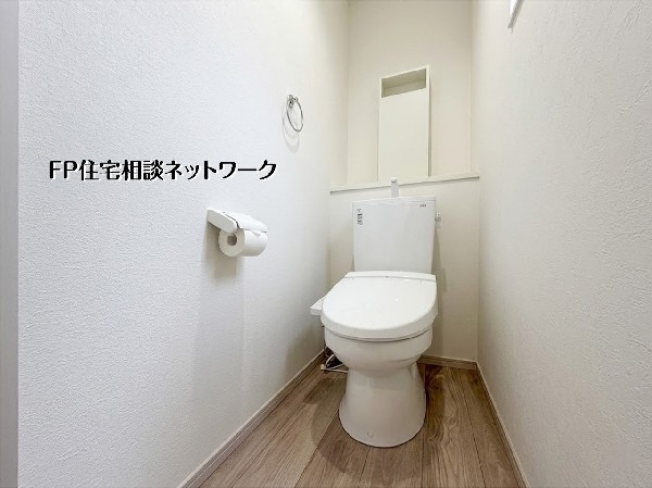【トイレ】清潔感あふれる白を基調としたトイレです。温水洗浄便座付きで、毎日を快適に過ごせます。木目調の床が温かみを添える心地よい空間。奥には便利な棚もあり、小物もすっきり収納可能です。