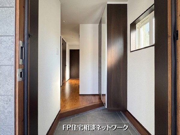 【玄関】  落ち着いた木目調の床と白い壁が調和する、清潔感あふれる玄関です。大容量のシューズボックスを備え、空間を美しく保てます。小窓からの自然光が差し込む明るい設計です。