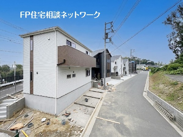 外観:【外観│車2台】白い外壁にブラウンのバルコニーが特徴的な2階建て住宅の外観です。前面道路に面し、外構部分は施工中の状態です。周辺には同様の新しい住宅が建ち並んでいます。