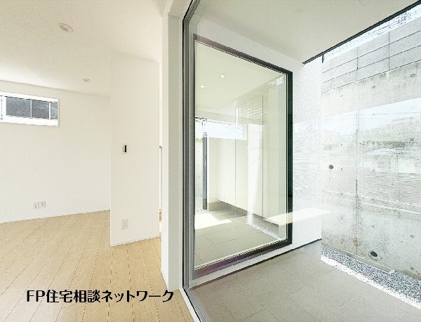 【中庭】  室内から望む、明るい光が差し込む玄関土間スペース。ガラス越しに見えるコンクリートの打ちっぱなしの壁が、シンプルで洗練された空間を演出しています。雨の日でも快適なインナーガレージへの動線も魅力。