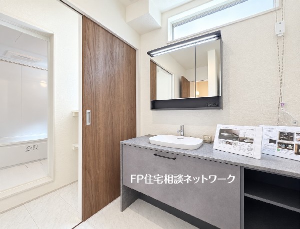 【洗面脱衣室】  幅が広く使いやすい洗面化粧台を備えた洗面脱衣スペースです。グレーの天板がお洒落で、鏡の裏や下部には収納スペースも充実。引き戸を採用しており、限られた空間でもスムーズに出入り可能です。